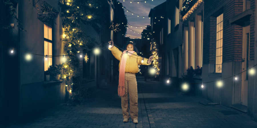 Meisje houdt een lichtslinger vast en staat in het midden van een feëriek verlichte straat Meisje houdt een lichtslinger vast en staat in het midden van een feëriek verlichte straat